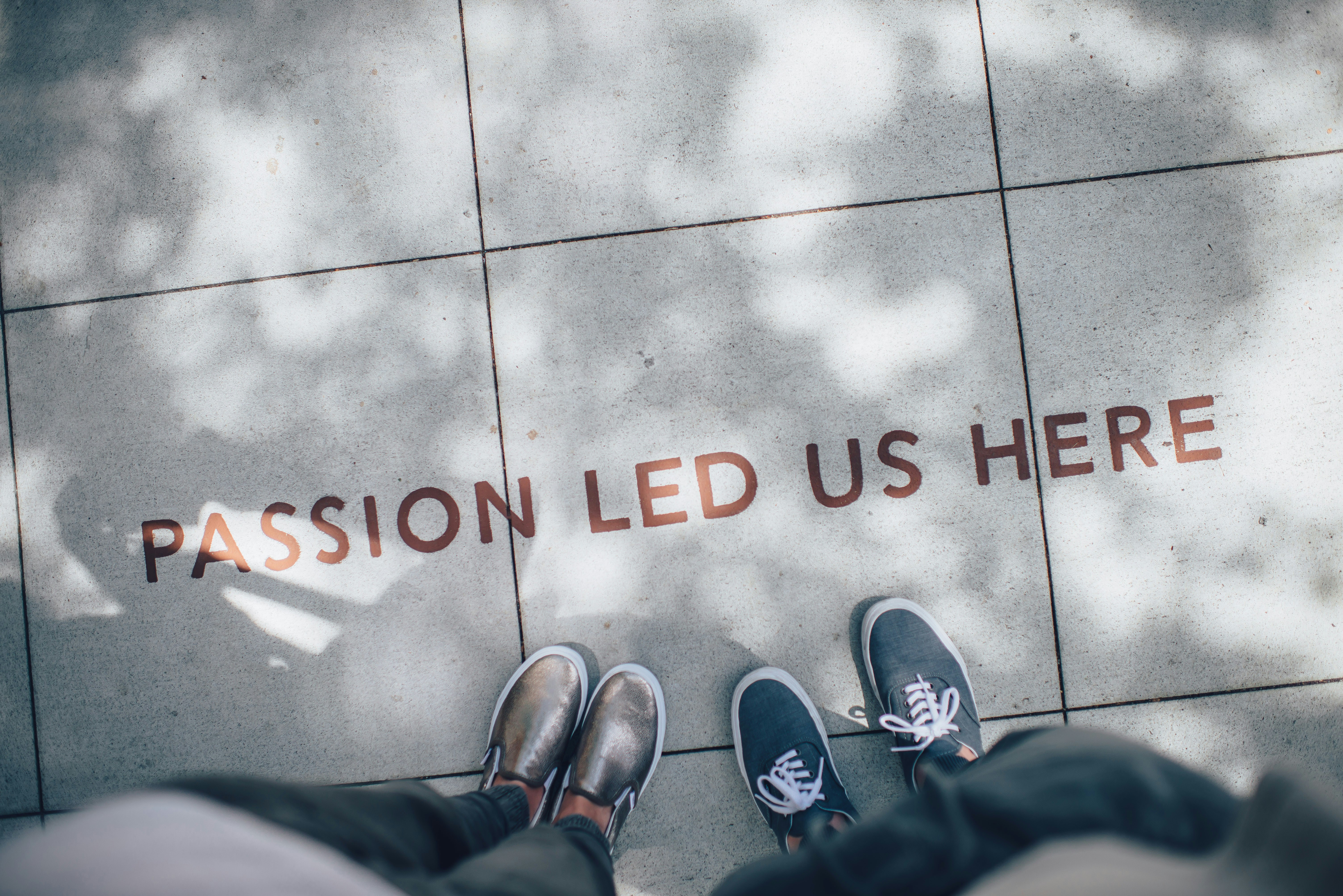 Photo of two pairs of feet wearing different tennis shoes next to writing on the pavement that says Passion Led Us Here